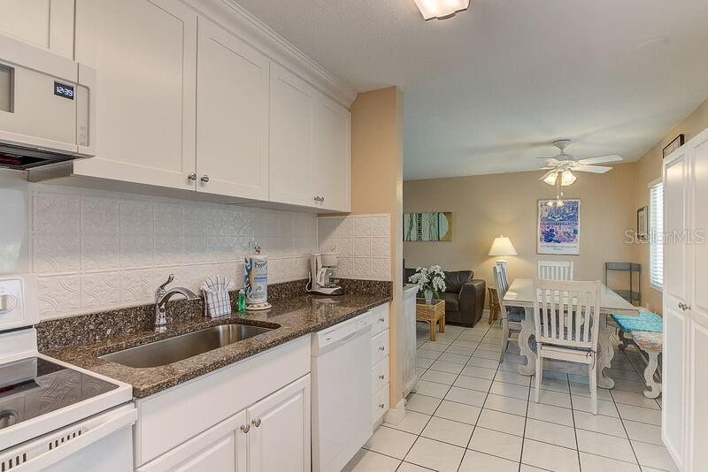 A white kitchen with granite countertops overlooks a dining area and living room — 6020 MIDNIGHT PASS ROAD UNIT 1, SARASOTA, FL
