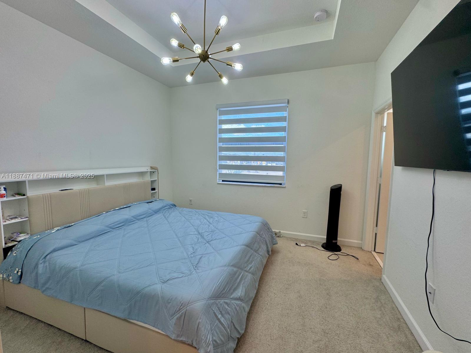 A bedroom features a blue bed, a modern chandelier, a window, and a wall-mounted television — 23541 SW 127th Pl, Homestead FL 33032, HOMESTEAD, FL