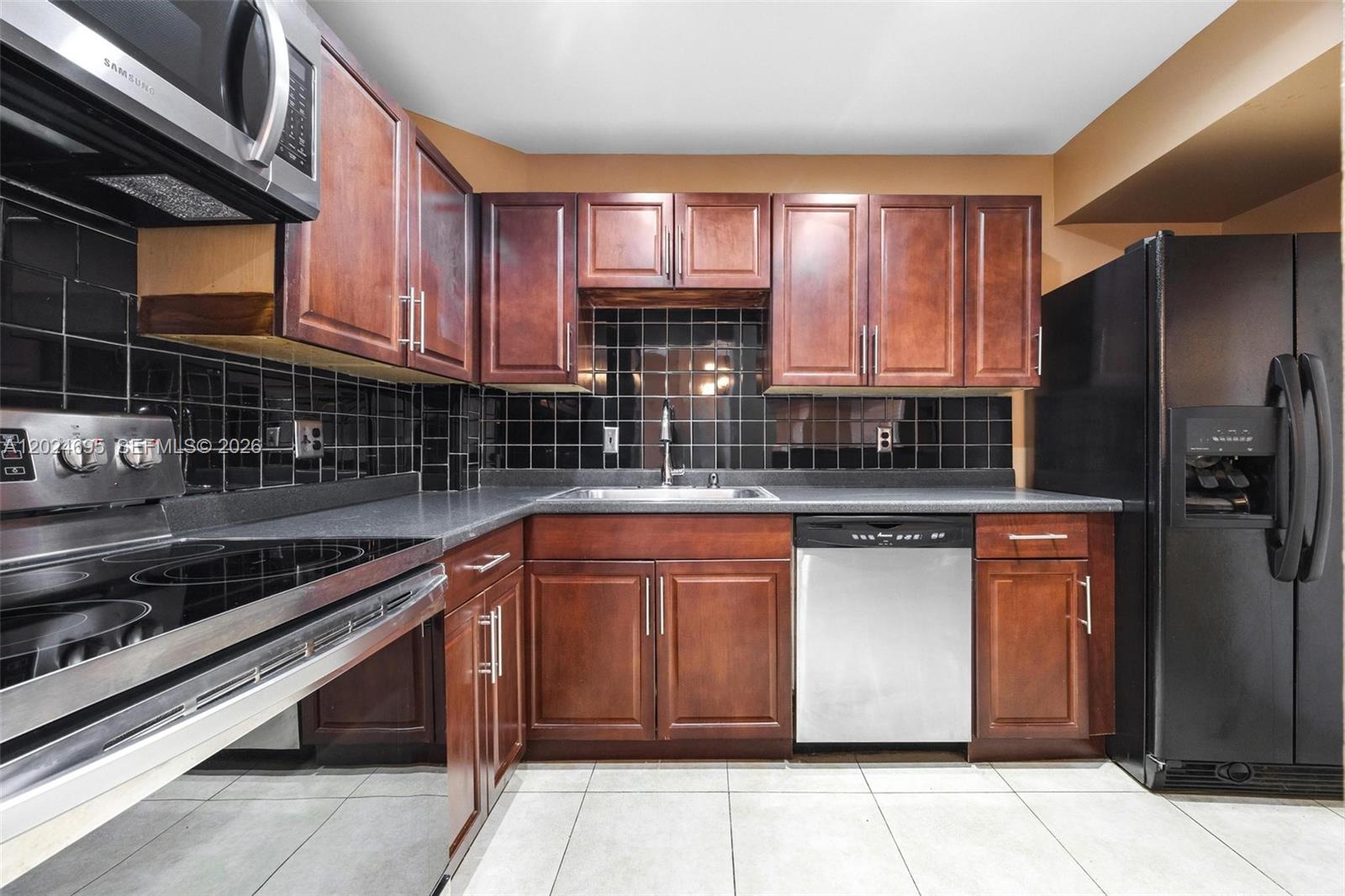 A kitchen features dark wood cabinets, black tile backsplash, stainless steel appliances, and tile flooring — 4350 Hillcrest Dr # 1016, Hollywood FL 33021, HOLLYWOOD, FL