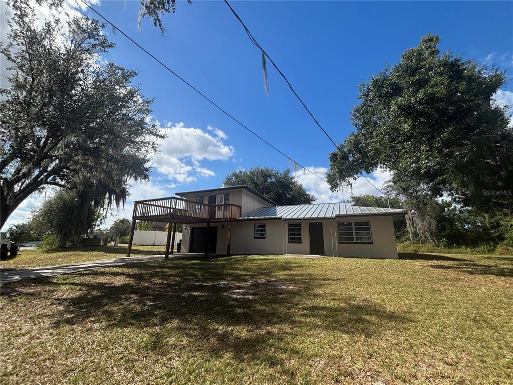 A two-story house with a wooden deck, metal roof, and large surrounding trees — 127 JAMISON AVENUE, LAKE PLACID, FL