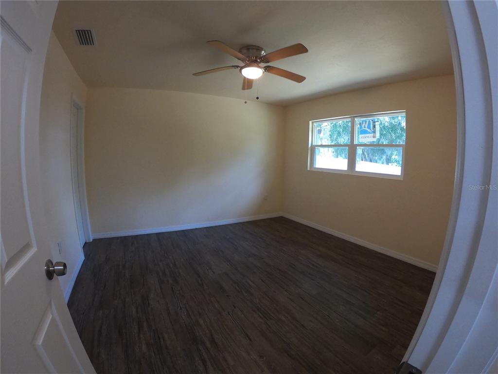 An empty bedroom features light-colored walls, dark wood-look flooring, and a ceiling fan — 127 JAMISON AVENUE, LAKE PLACID, FL