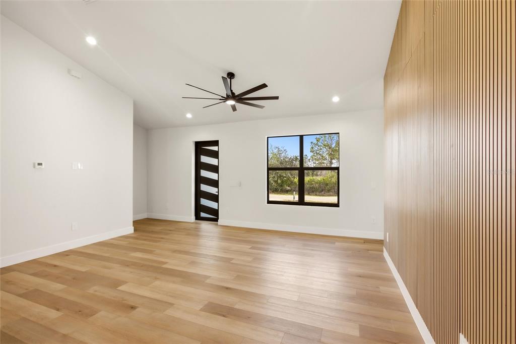 A modern room features light wood flooring, a slatted wood accent wall, and a ceiling fan — 7322 GRANADA BOULEVARD, SEBRING, FL