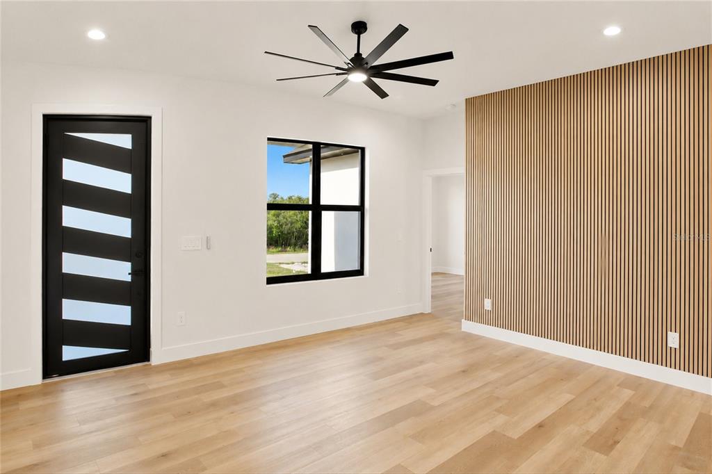 A room with light wood flooring, a slatted wood accent wall, and a black door — 7322 GRANADA BOULEVARD, SEBRING, FL