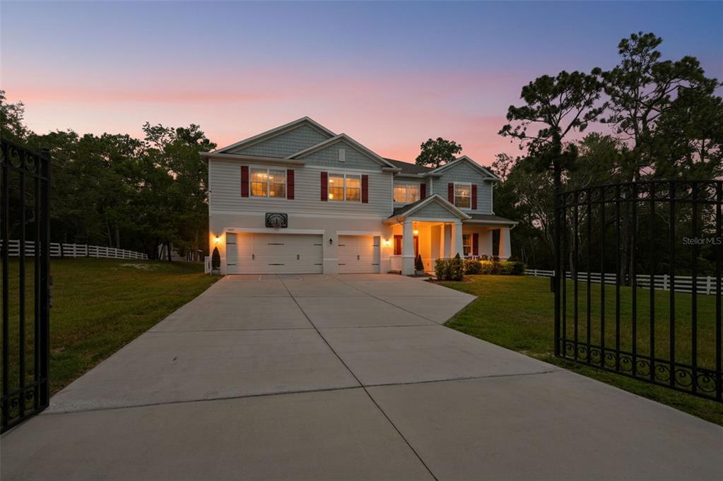 A two-story suburban house with a three-car garage and a gated concrete driveway at dusk — 9025 MAZETTE ROAD, WEEKI WACHEE, FL