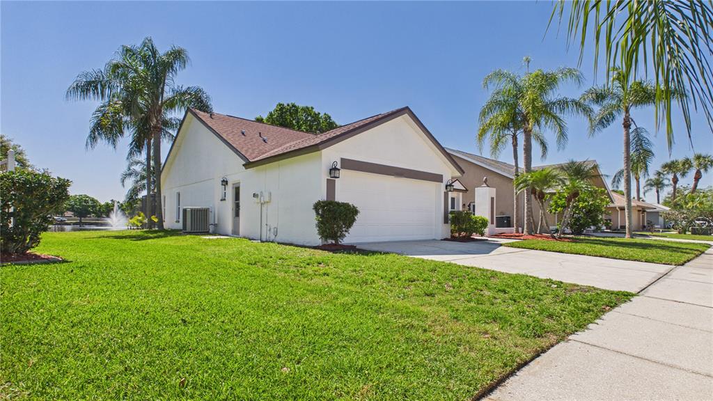 A white single-story house with a two-car garage, lawn, and palm trees under a blue sky — 8609 BOYSENBERRY DRIVE, TAMPA, FL