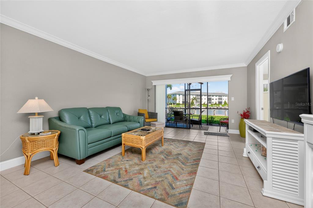A living room features a teal sofa, a patterned rug, and a sliding glass door — 3670 BAL HARBOR BOULEVARD UNIT 1F, PUNTA GORDA, FL