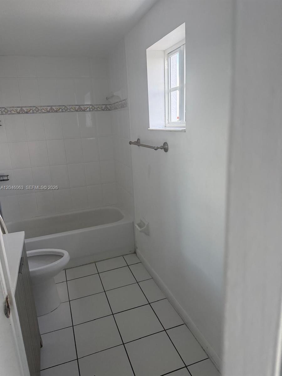 A bathroom features a white tiled bathtub, a toilet, and a window with white walls — 21 E 3rd St # 405, Hialeah FL 33010, HIALEAH, FL