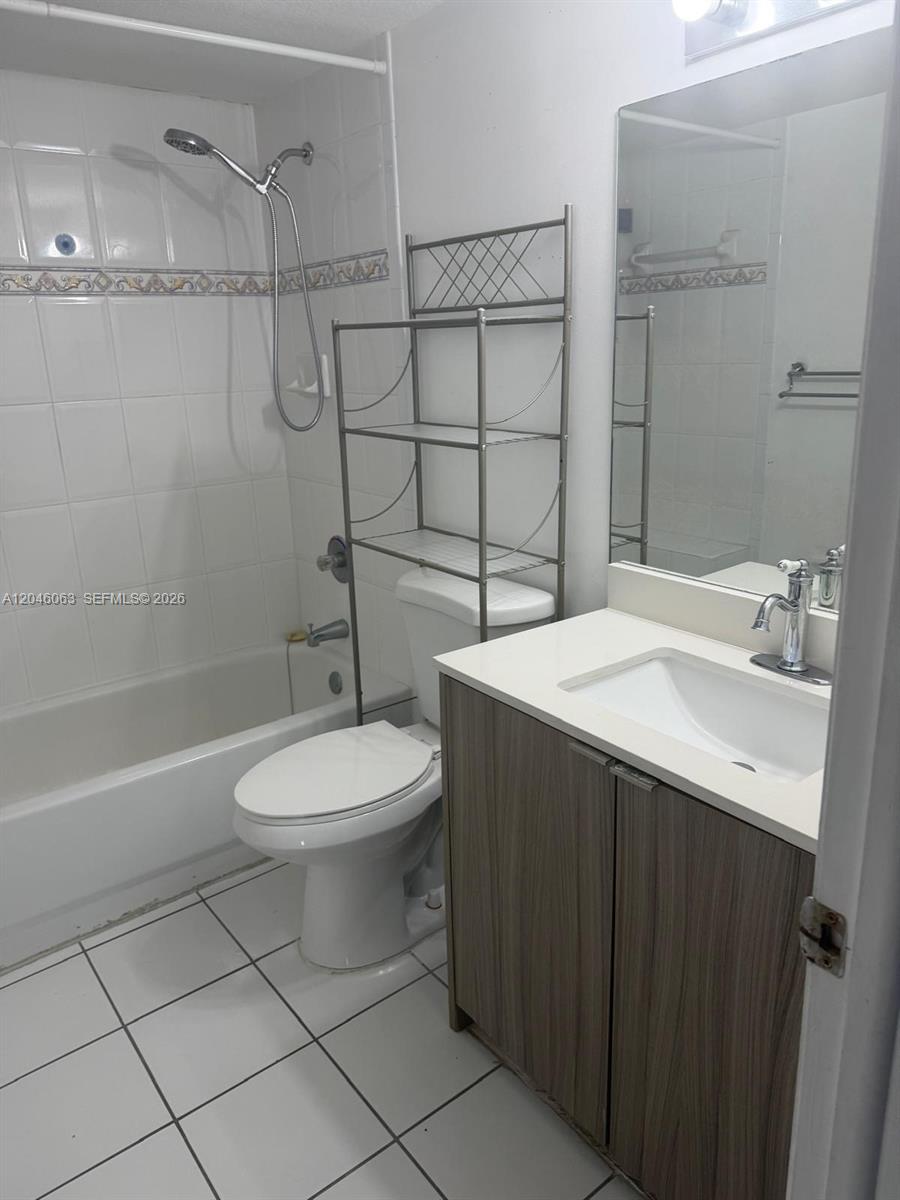 A bathroom features a white tub-shower combo, a toilet with a metal shelf, and vanity — 21 E 3rd St # 405, Hialeah FL 33010, HIALEAH, FL