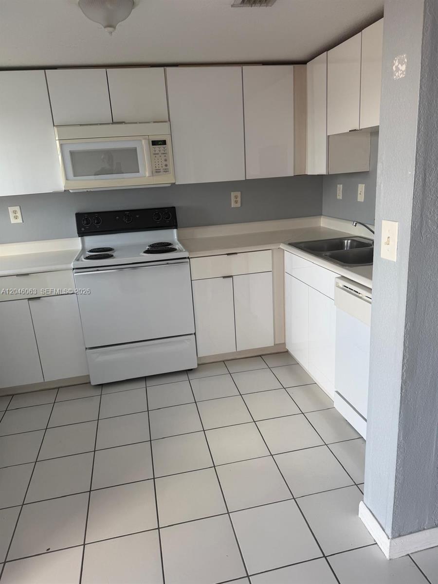 A kitchen features white cabinets, white appliances, a double sink, and light-colored tile flooring — 21 E 3rd St # 405, Hialeah FL 33010, HIALEAH, FL