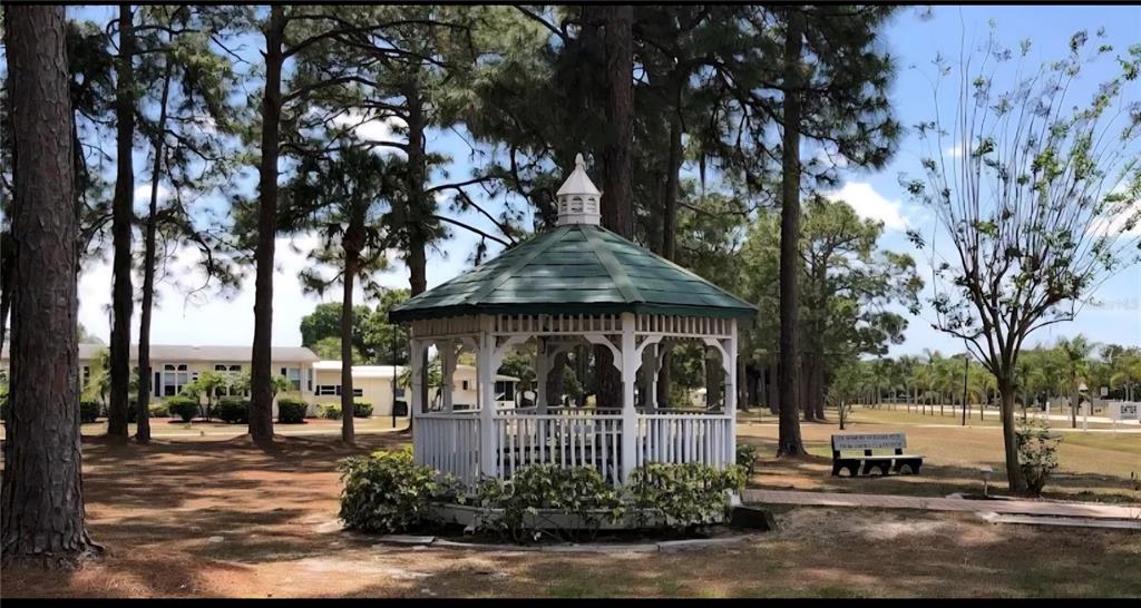 A white gazebo with a green roof sits in a grassy area with pine trees — 6789 HAKI COURT, NORTH PORT, FL