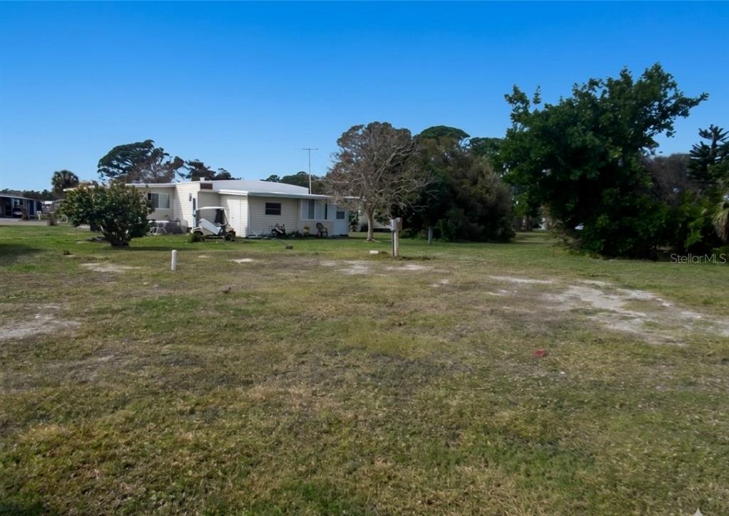 A single-story house sits on a large, grassy lot with trees under a clear sky — 6789 HAKI COURT, NORTH PORT, FL