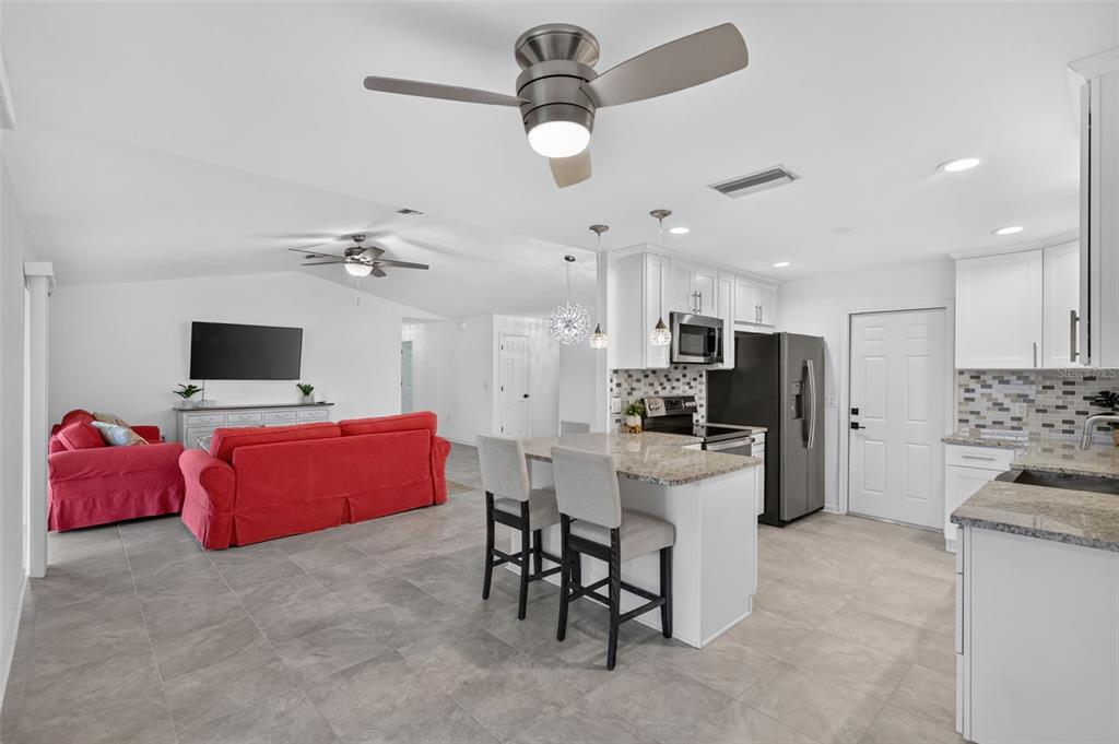 An open-concept kitchen and living area with white cabinets, a red sofa, and tile flooring — 4063 PALAU DRIVE, SARASOTA, FL