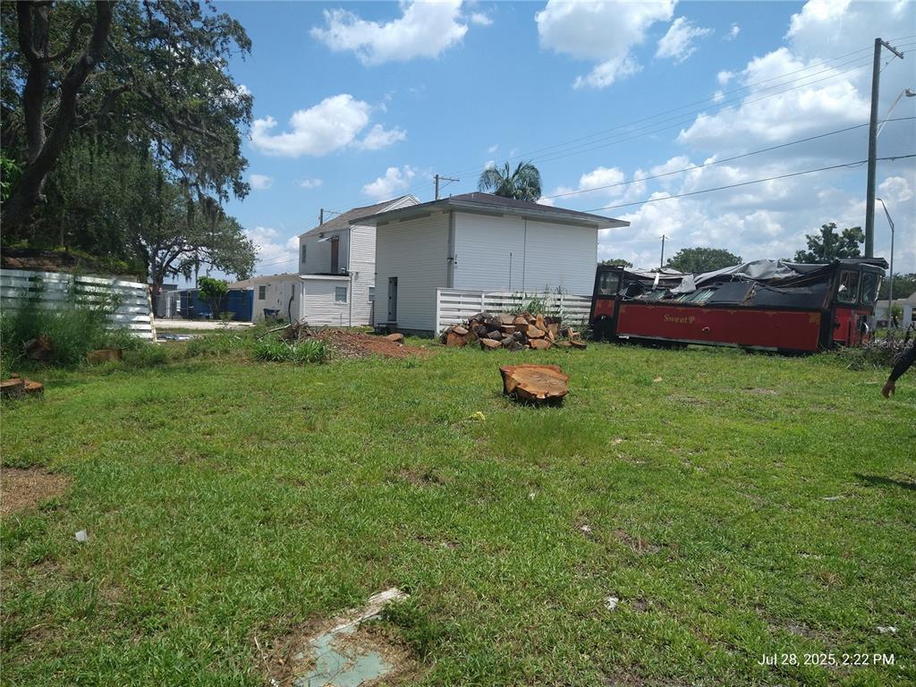 A grassy lot features a white building, a pile of logs, and a red trolley — 909 and 911 WEST HILLSBOROUGH AVENUE, TAMPA, FL