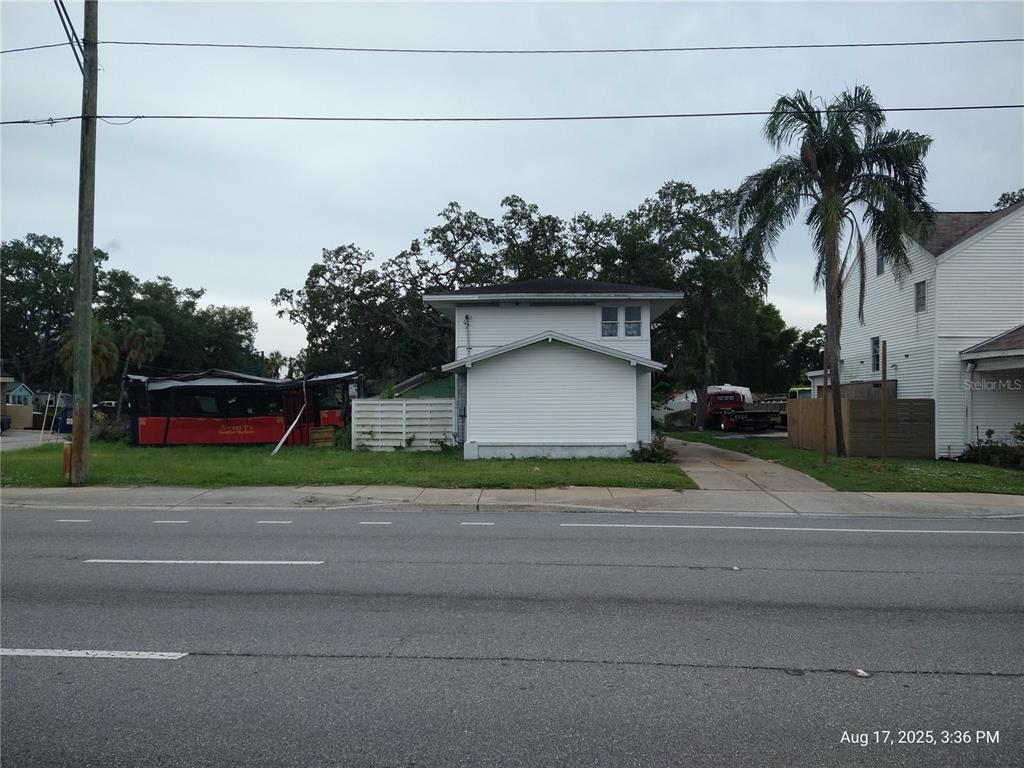 A white two-story house stands next to a red bus on a grassy lot — 909 and 911 WEST HILLSBOROUGH AVENUE, TAMPA, FL
