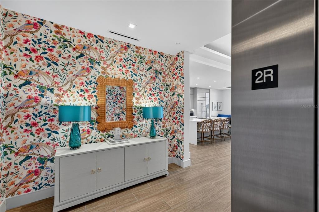A hallway features floral wallpaper, a white console table with blue lamps, and an elevator door — 1591 GULF OF MEXICO DRIVE UNIT 216, LONGBOAT KEY, FL