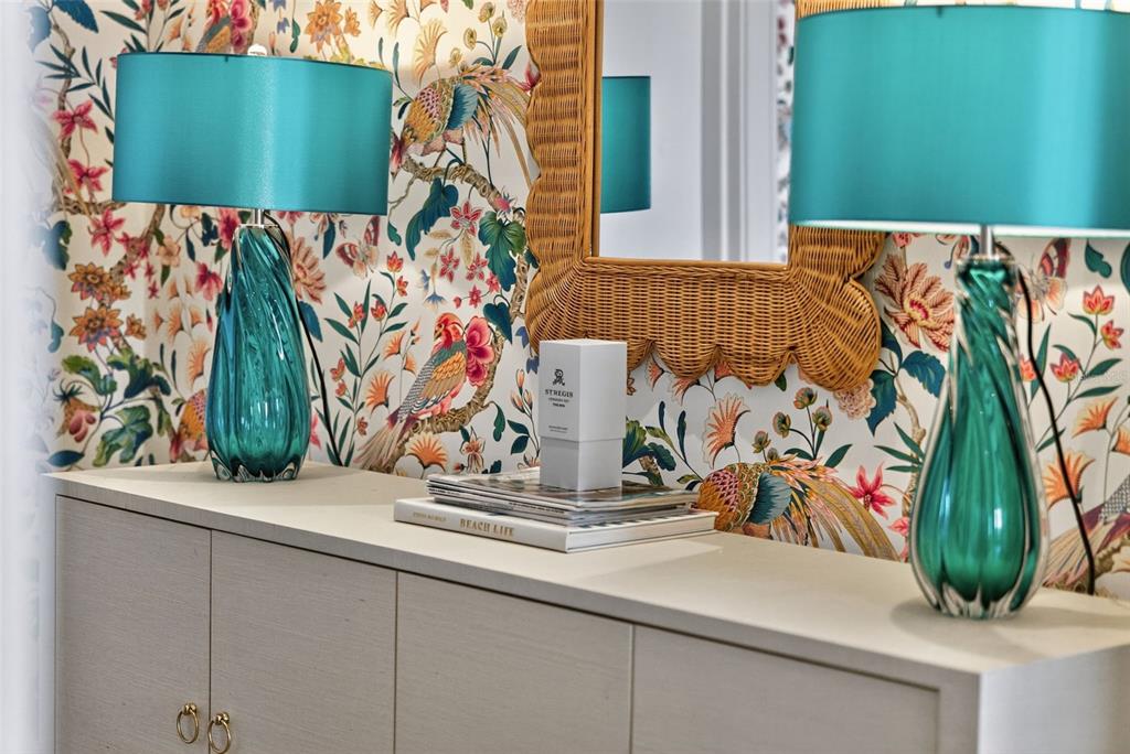 A console table with two teal lamps sits against floral wallpaper and a wicker mirror — 1591 GULF OF MEXICO DRIVE UNIT 216, LONGBOAT KEY, FL