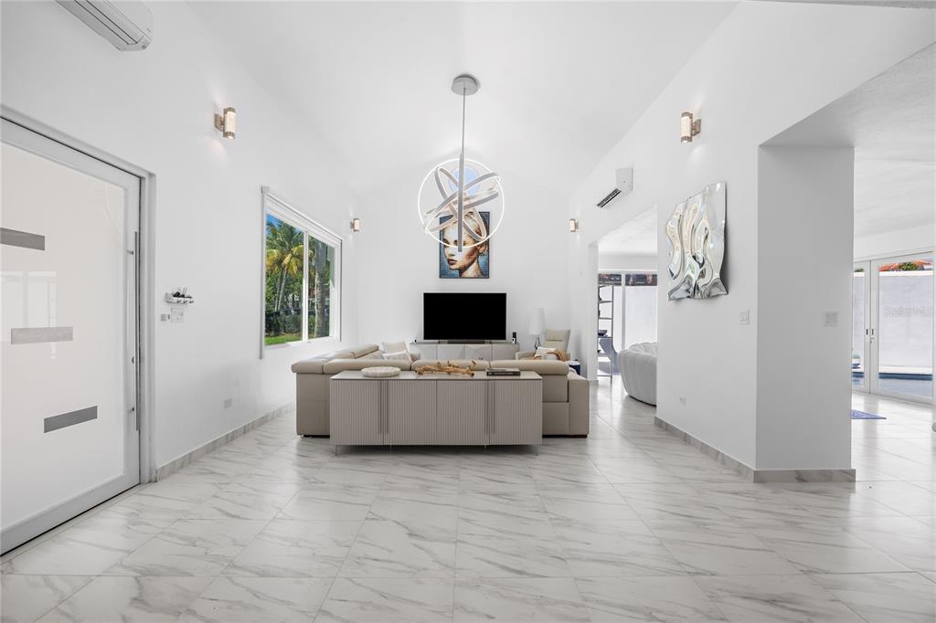 A bright living room features white marble floors, a vaulted ceiling, and a modern chandelier — 394 DORADO BEACH EAST, DORADO, PR