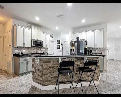 A kitchen features white cabinets, a stone-faced island with two stools, and wood-look tile flooring — 911 LA TERRAZA LANE, KISSIMMEE, FL