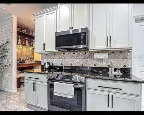A kitchen features white cabinets, a stainless steel microwave, and a dark countertop — 911 LA TERRAZA LANE, KISSIMMEE, FL