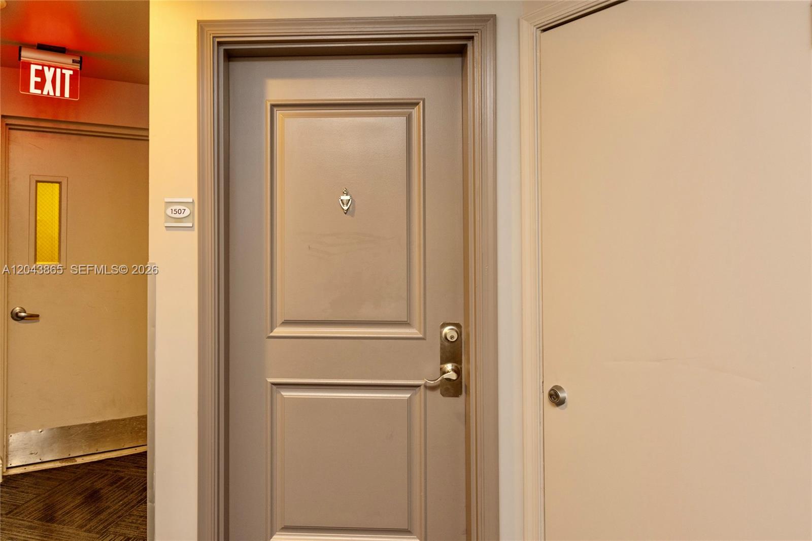 A hallway features a central door with a peephole and a nearby exit sign — 480 NE 30th St # 1507, Miami FL 33137, MIAMI, FL