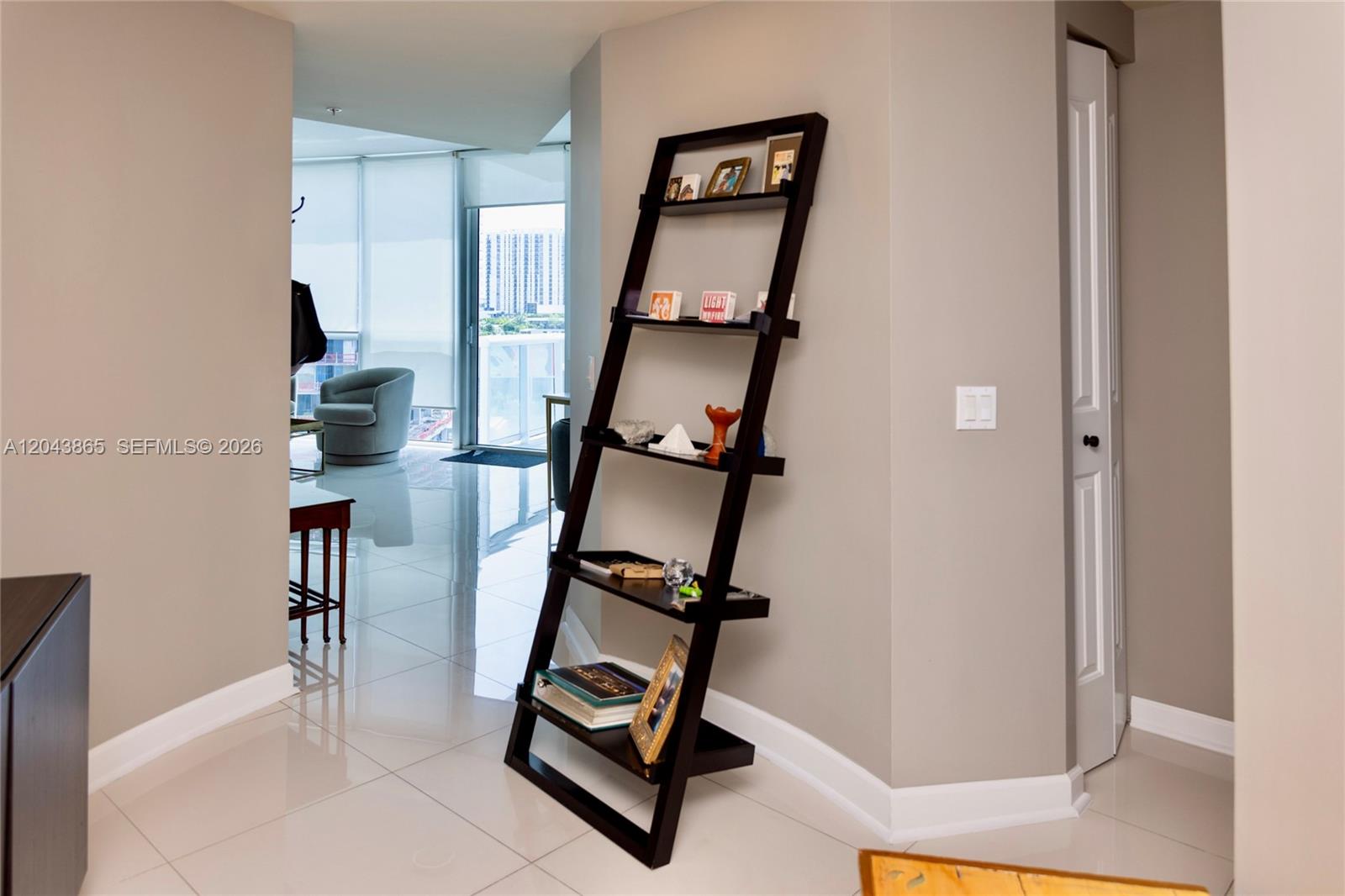 A dark wood leaning bookshelf stands in a hallway with white tile flooring — 480 NE 30th St # 1507, Miami FL 33137, MIAMI, FL