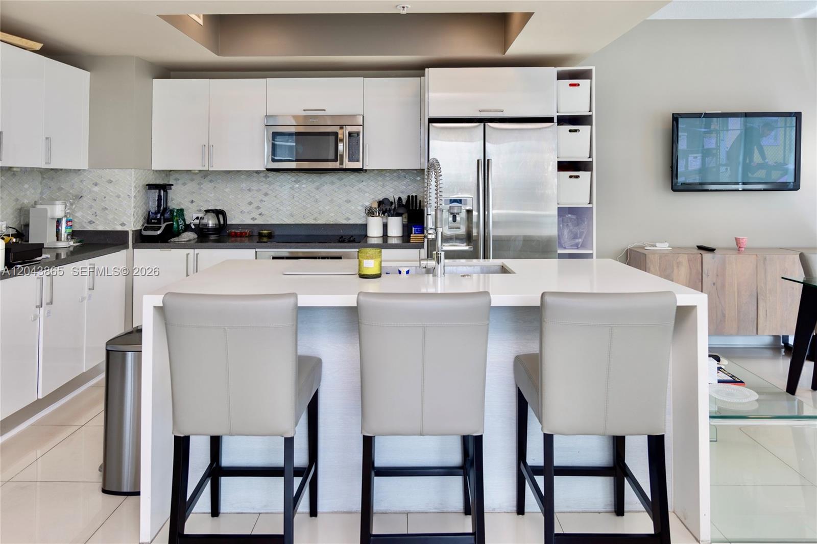 A modern kitchen features white cabinetry, stainless steel appliances, a central island, and three chairs — 480 NE 30th St # 1507, Miami FL 33137, MIAMI, FL