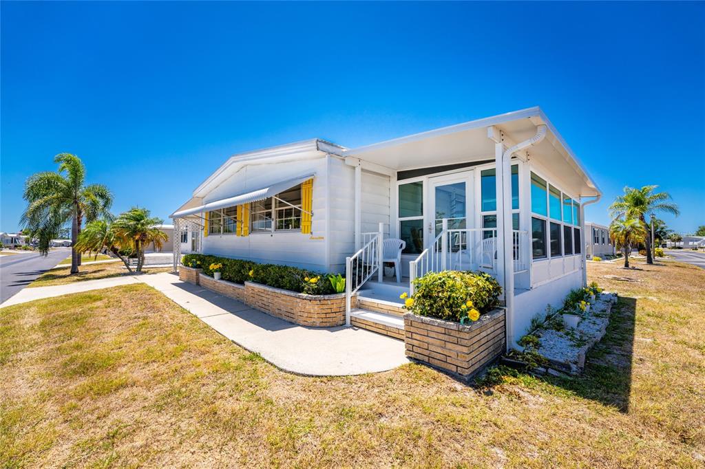 A white mobile home features a screened-in porch, brick planters, and yellow window awnings — 17 N FLORA VISTA STREET, ENGLEWOOD, FL