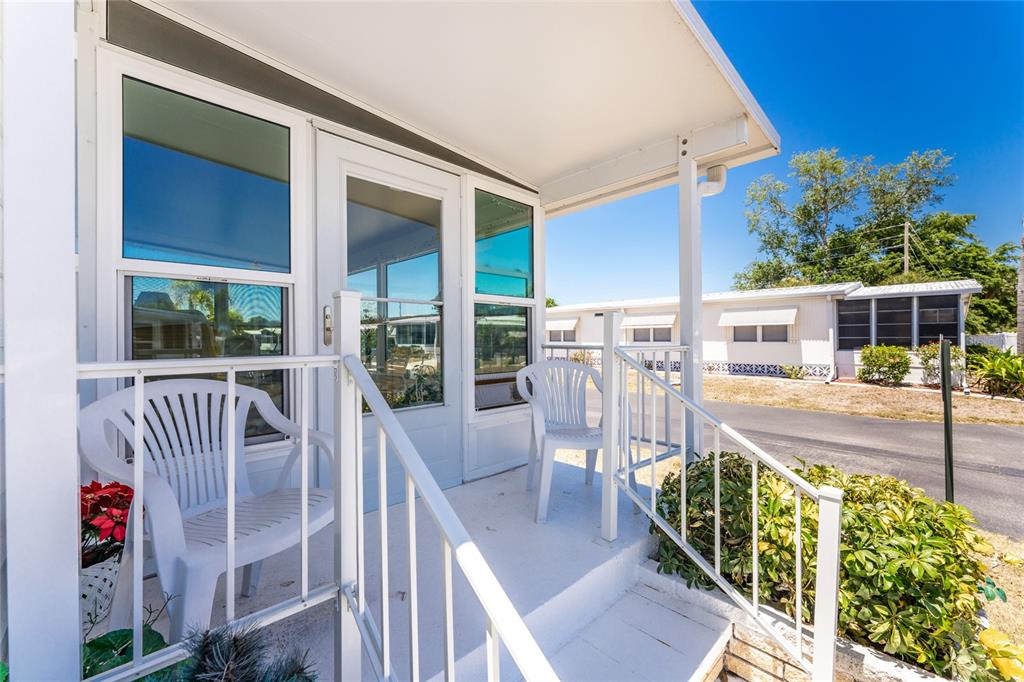 A white mobile home features a small covered porch with white railings and two plastic chairs — 17 N FLORA VISTA STREET, ENGLEWOOD, FL