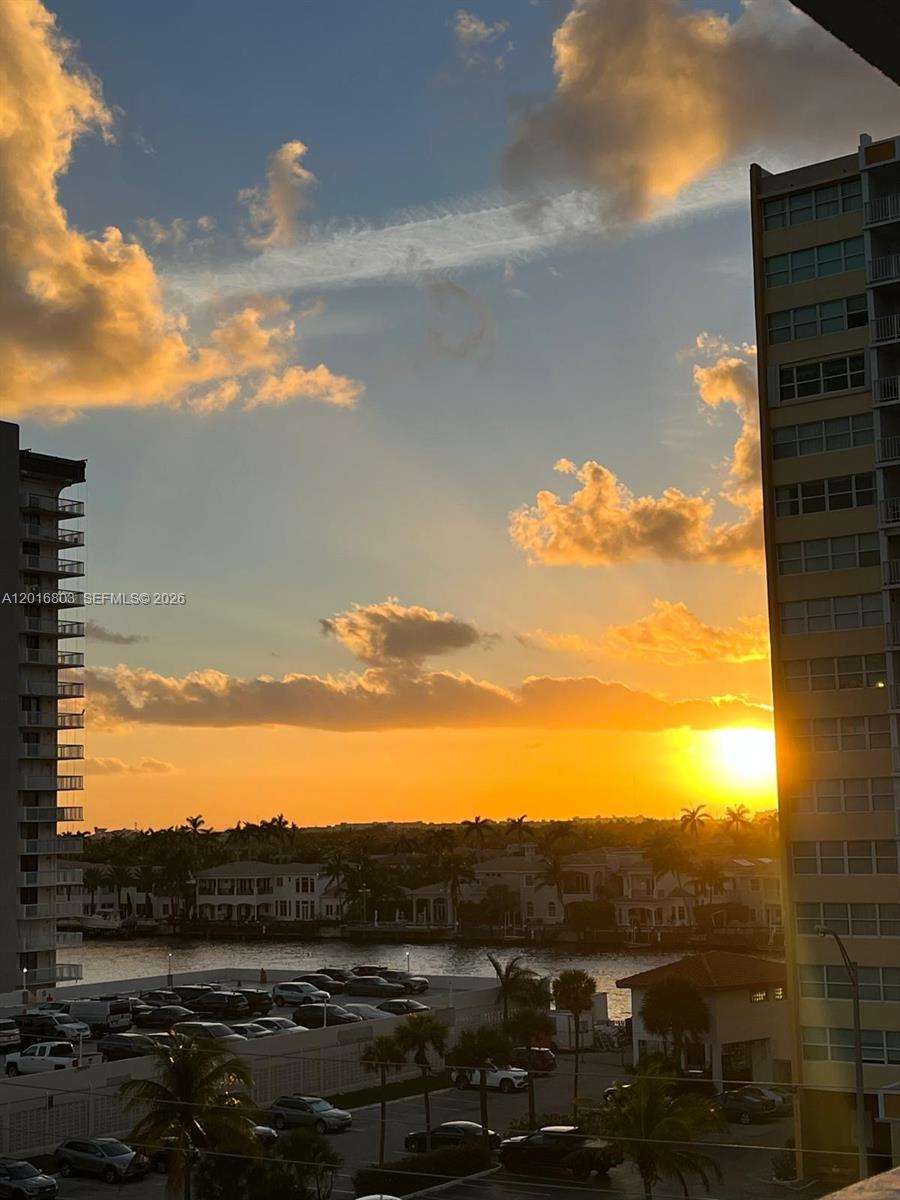 An exterior view shows a sunset over a waterway with buildings and parked cars below — 1601 S Ocean Dr # 605, Hollywood FL 33019, HOLLYWOOD, FL