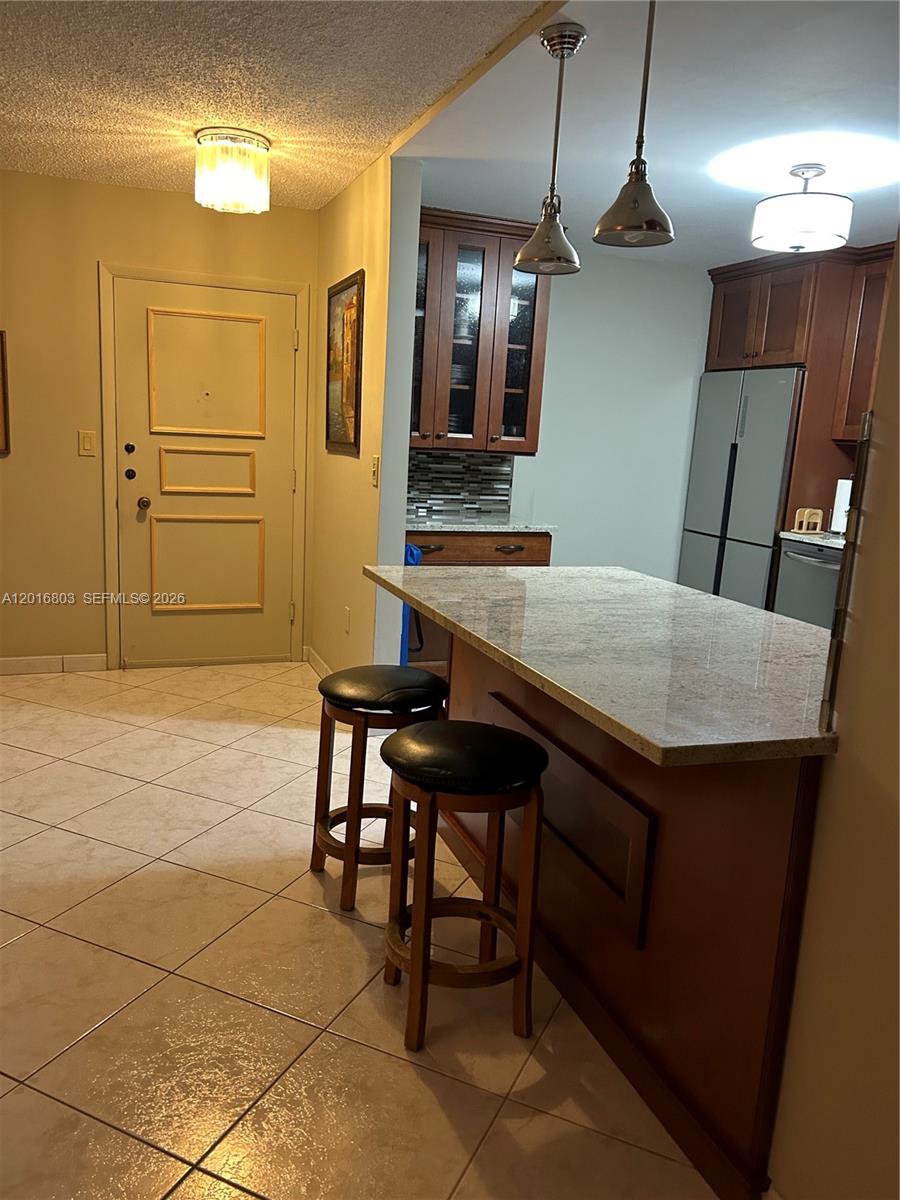 A kitchen features a granite-topped island, wooden cabinets, stainless steel appliances, and tile flooring — 1601 S Ocean Dr # 605, Hollywood FL 33019, HOLLYWOOD, FL