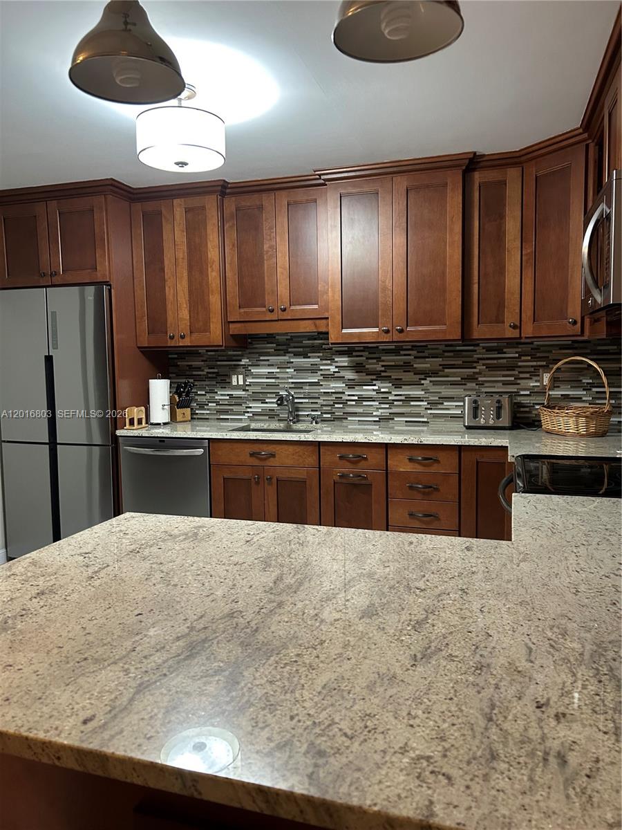 A kitchen features wooden cabinets, granite countertops, a tiled backsplash, and stainless steel appliances — 1601 S Ocean Dr # 605, Hollywood FL 33019, HOLLYWOOD, FL