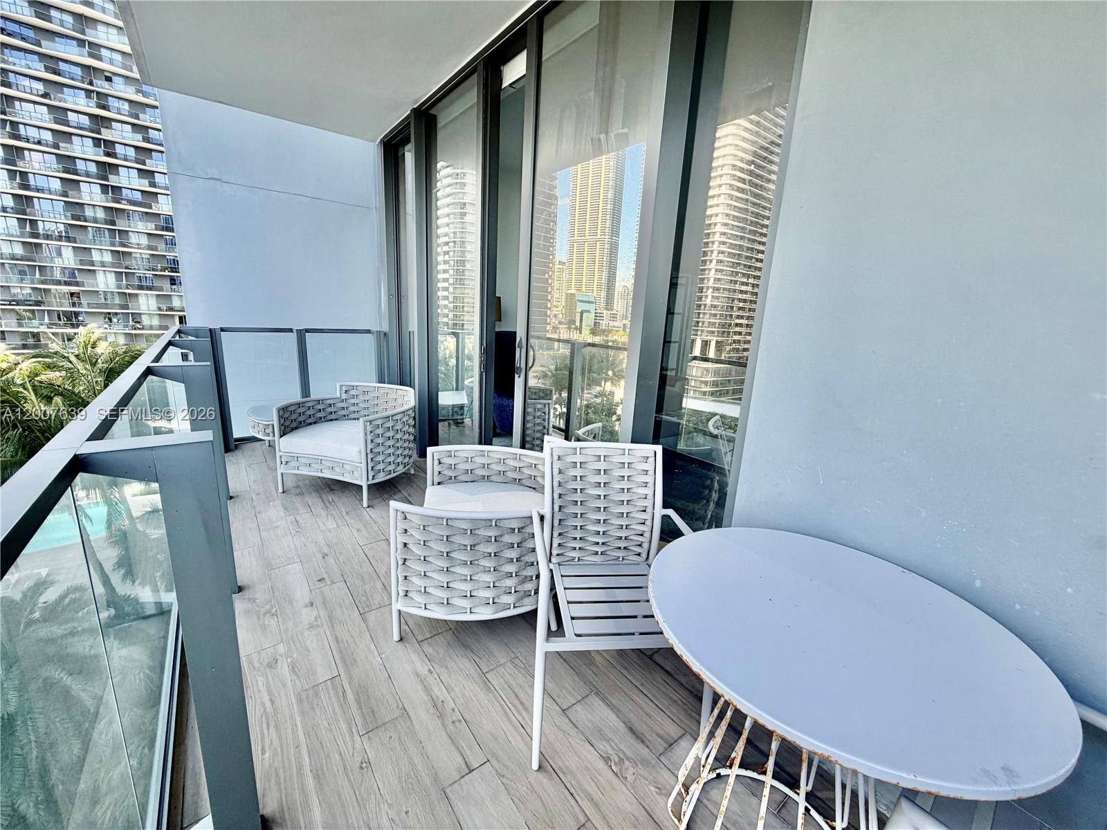 A balcony with light wood-look tile flooring, white woven chairs, and a small round table — 88 SW 7th St # 1109, Miami FL 33130, MIAMI, FL