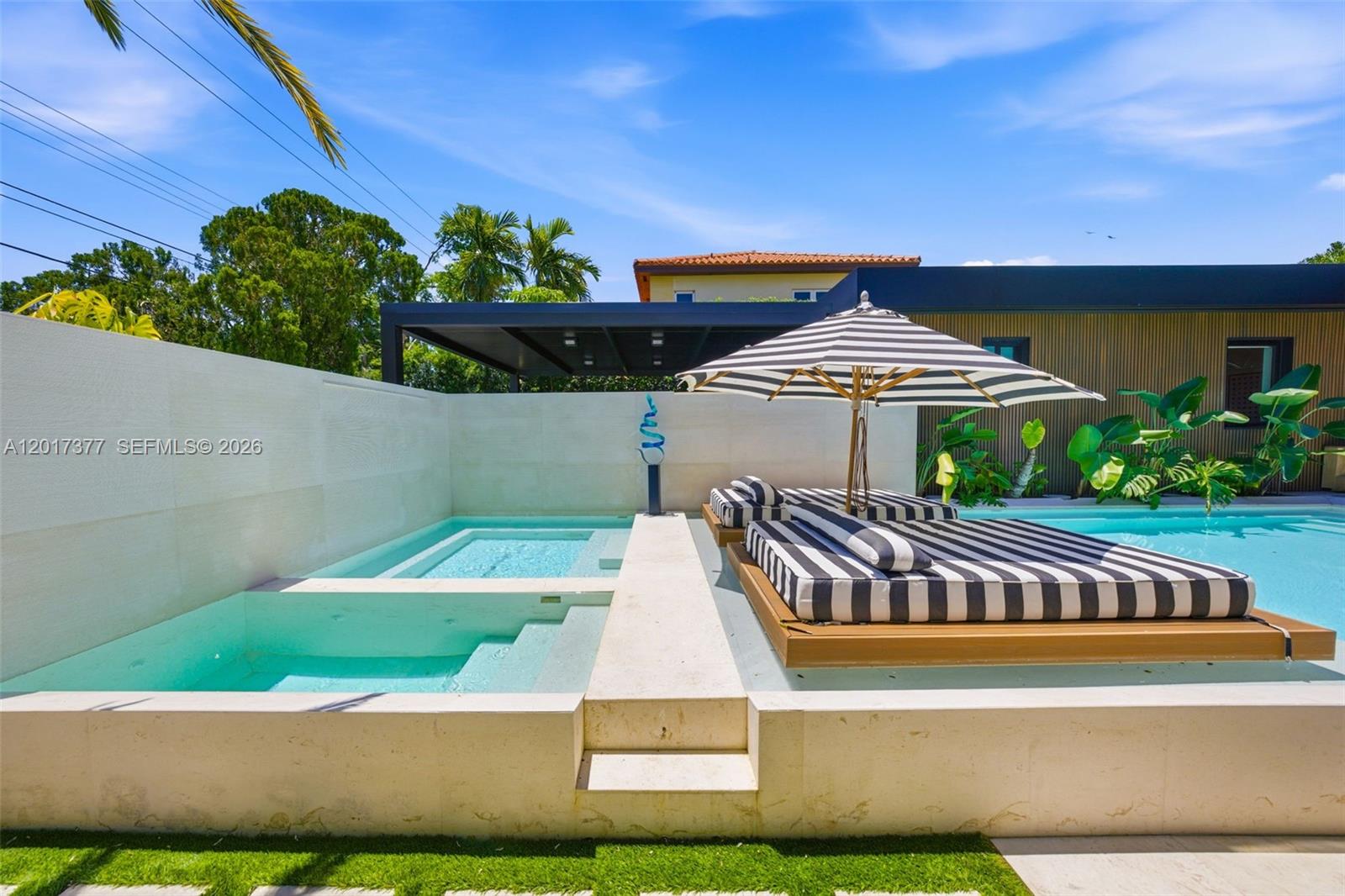 A swimming pool features a built-in lounge area with striped cushions and a matching umbrella — 5750 La Gorce Dr, Miami Beach FL 33140, MIAMI BEACH, FL