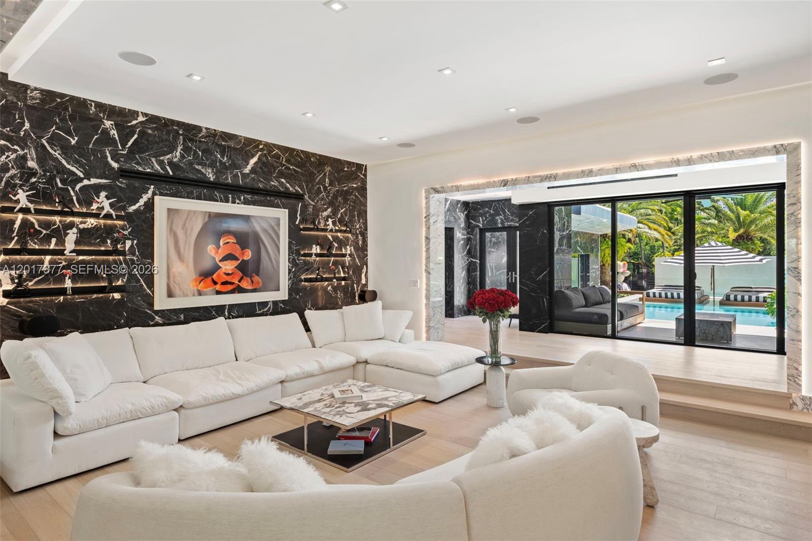A modern living room features a black marble wall, white sectional sofas, and sliding glass doors — 5750 La Gorce Dr, Miami Beach FL 33140, MIAMI BEACH, FL