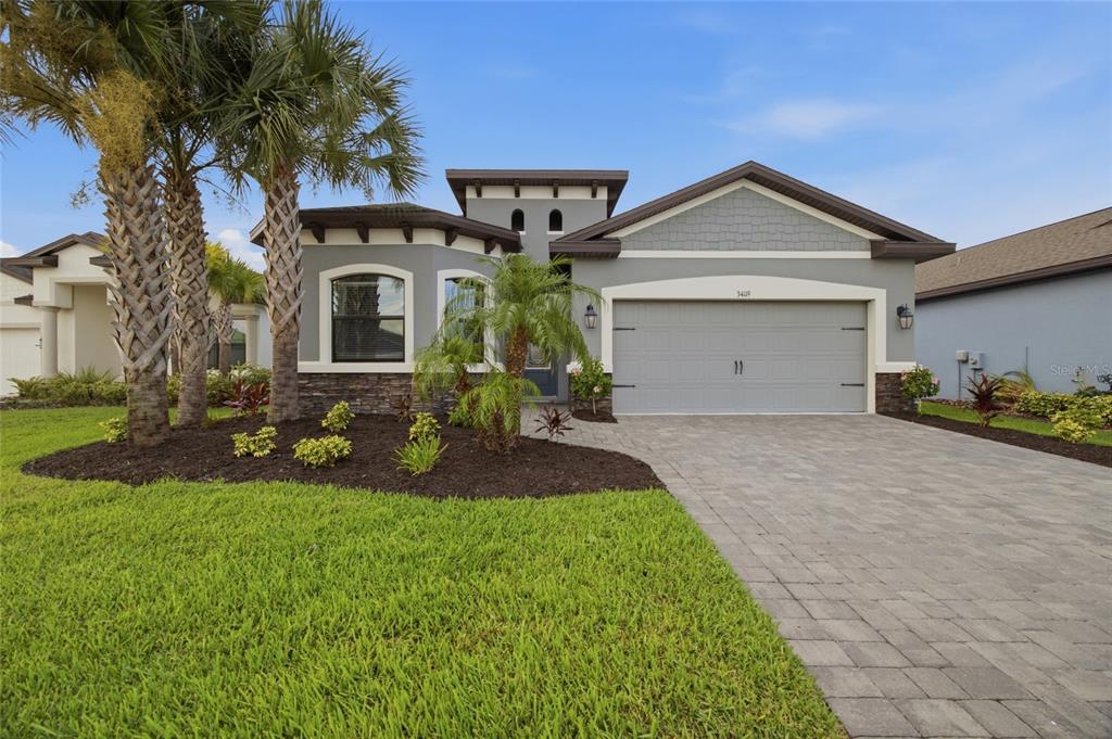 A single-story gray house with a stone base, a two-car garage, and palm trees — 34119 EVERGREEN HILL COURT, WESLEY CHAPEL, FL