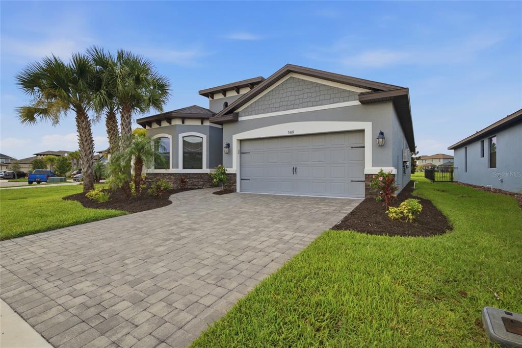 A gray single-story house with a paved driveway, stone accents, and a two-car garage — 34119 EVERGREEN HILL COURT, WESLEY CHAPEL, FL