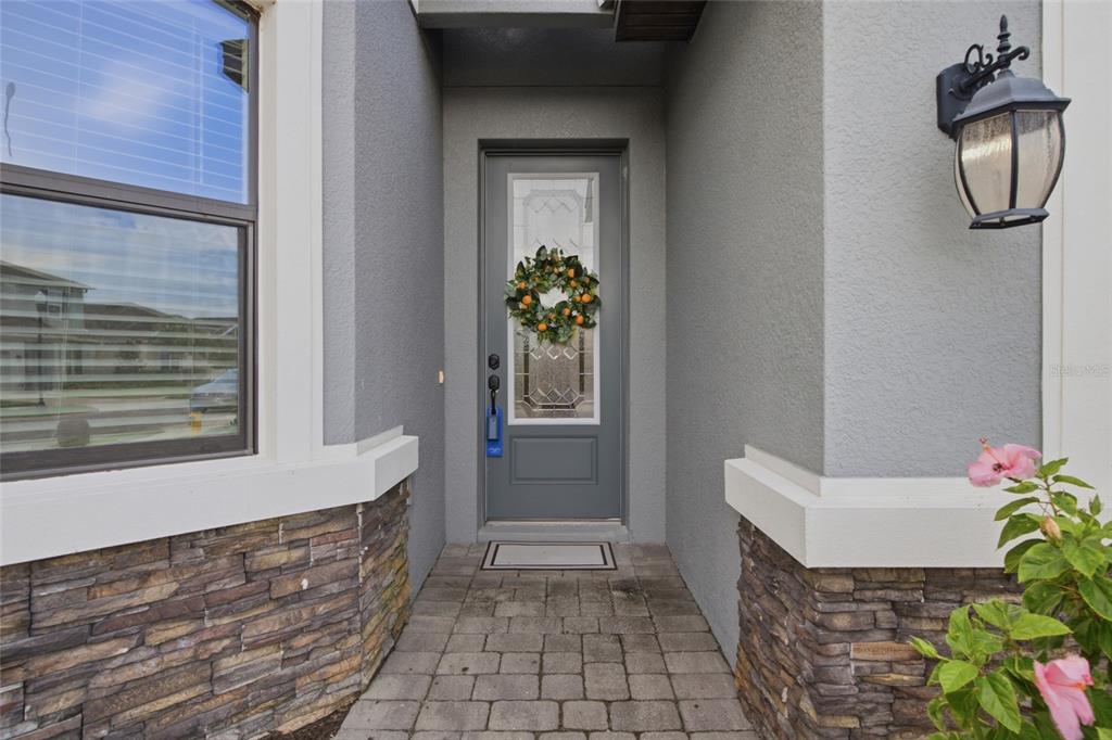 A gray front door with a wreath sits in a stone-accented entryway with a lantern — 34119 EVERGREEN HILL COURT, WESLEY CHAPEL, FL