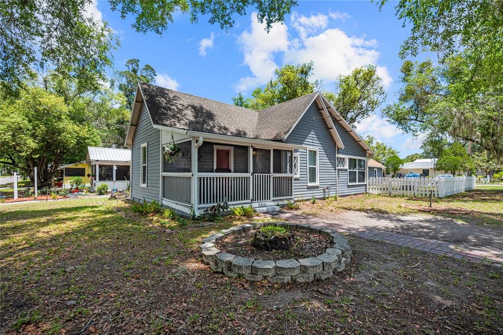 A gray, single-story house with a screened front porch and a circular stone garden bed — 5416 8TH STREET, ZEPHYRHILLS, FL