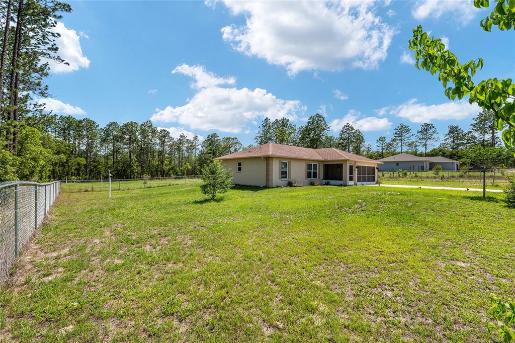 A tan single-story house with a screened porch sits on a large, fenced grassy lot — 13130 SW 76TH LANE, DUNNELLON, FL