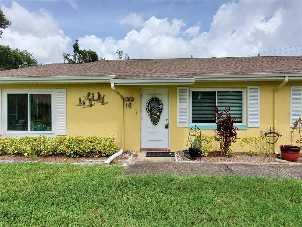 A yellow single-story house features a white front door, shuttered windows, and a grassy lawn — 1907 CANTERBURY LANE UNIT 14, SUN CITY CENTER, FL