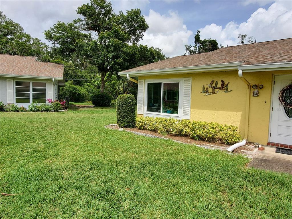 A yellow house exterior features a white front door, a large window, and landscaping — 1907 CANTERBURY LANE UNIT 14, SUN CITY CENTER, FL
