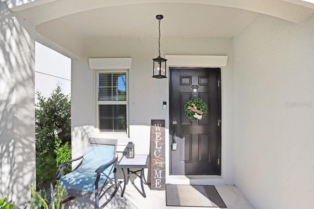 A covered front porch features a dark door, a rocking chair, and a welcome sign — 5426 RAINWOOD MEADOWS DRIVE, APOLLO BEACH, FL