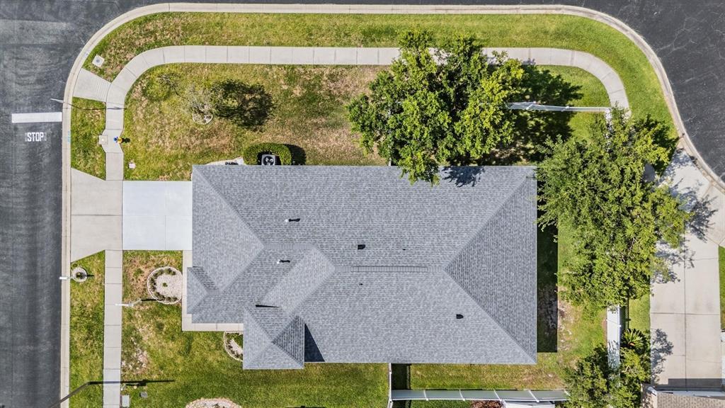 An aerial view shows a house with a gray shingled roof on a corner lot — 4940 WOODMERE ROAD, LAND O LAKES, FL