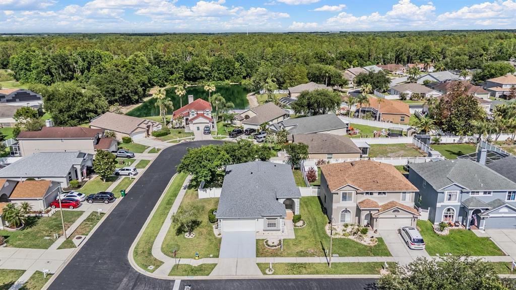 An aerial view shows a suburban neighborhood with single-family homes, a pond, and trees — 4940 WOODMERE ROAD, LAND O LAKES, FL