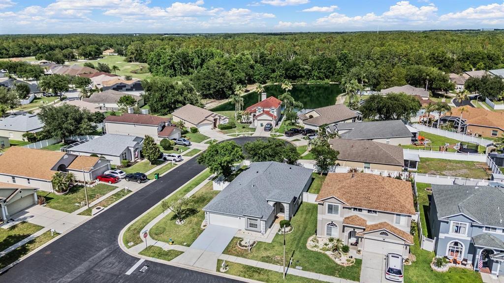 An aerial view shows suburban houses with driveways, lawns, and a pond in the background — 4940 WOODMERE ROAD, LAND O LAKES, FL
