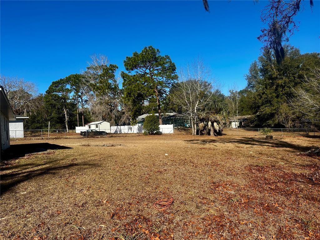 A large, grassy backyard features a white fence, mature trees, and a small shed — 606 WATER ROAD, OCALA, FL