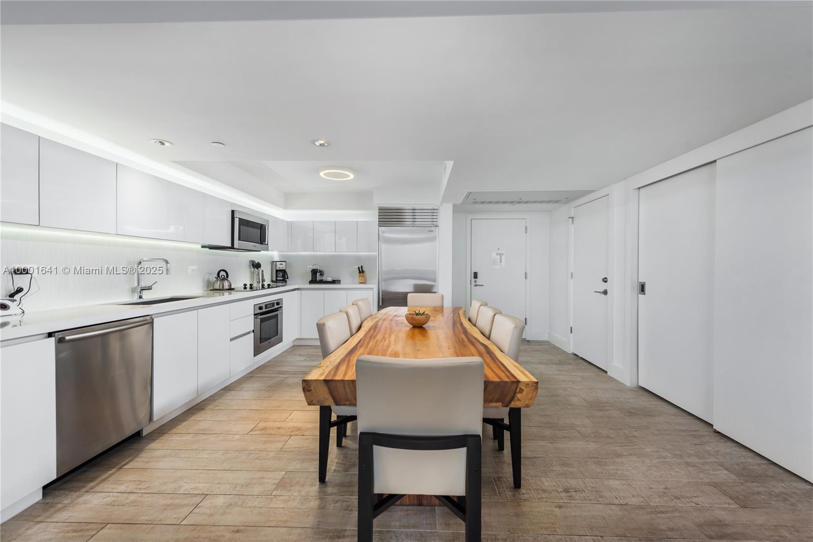 A modern kitchen features white cabinetry, stainless steel appliances, and a large live-edge dining table — 102 24 ST # 1040, Miami Beach FL 33139, MIAMI BEACH, FL