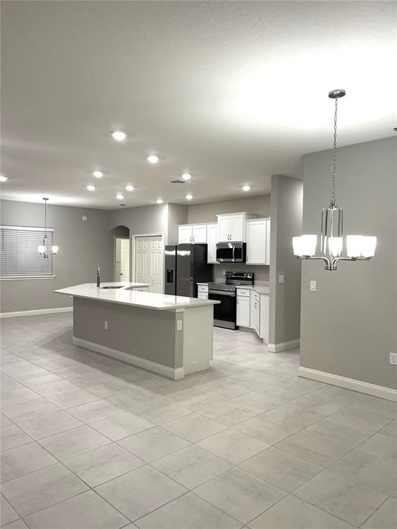 A kitchen features white cabinets, stainless steel appliances, a large island, and light tile flooring — 6783 TREYMONT DRIVE, LAKELAND, FL