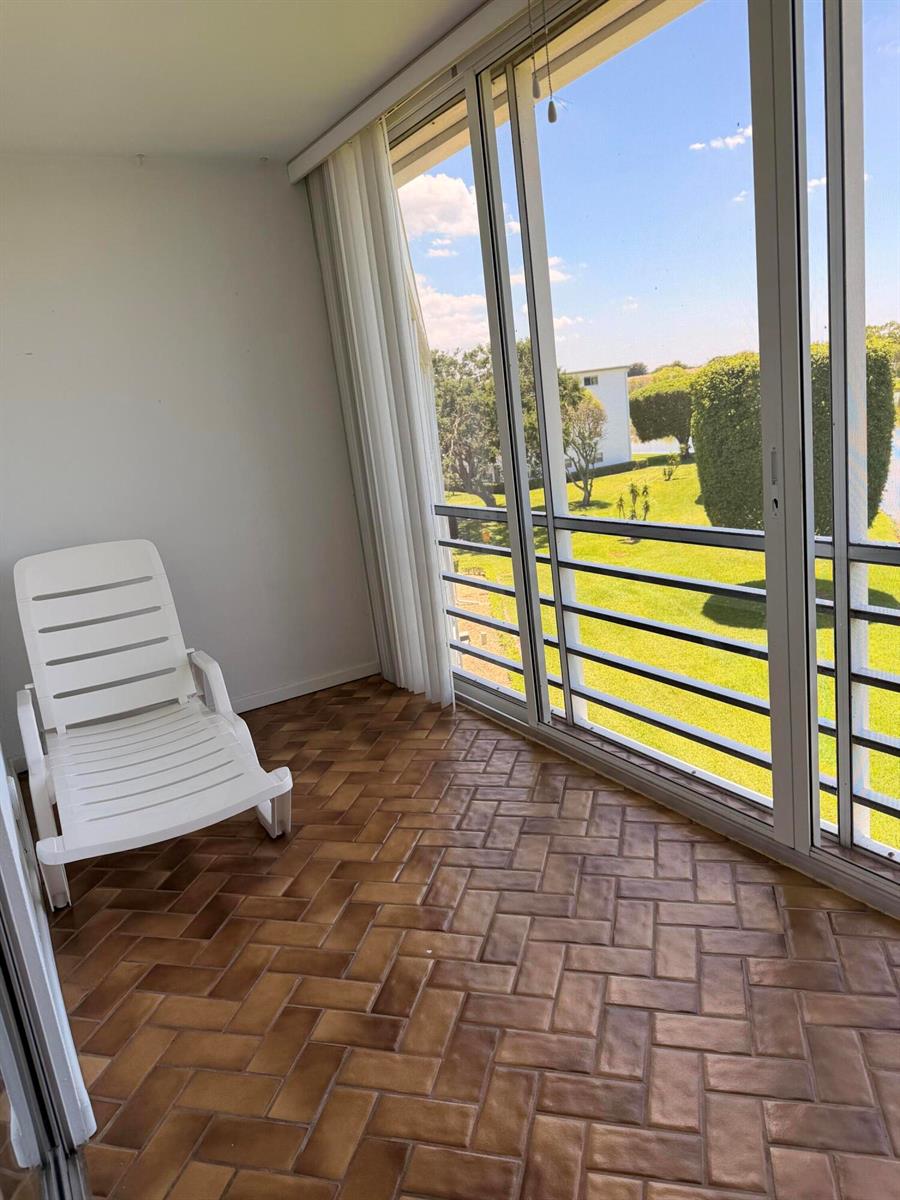 A sunroom with a white lounge chair, herringbone-patterned tile flooring, and sliding glass doors — 4074 Cornwall D, Boca Raton FL 33434, BOCA RATON, FL