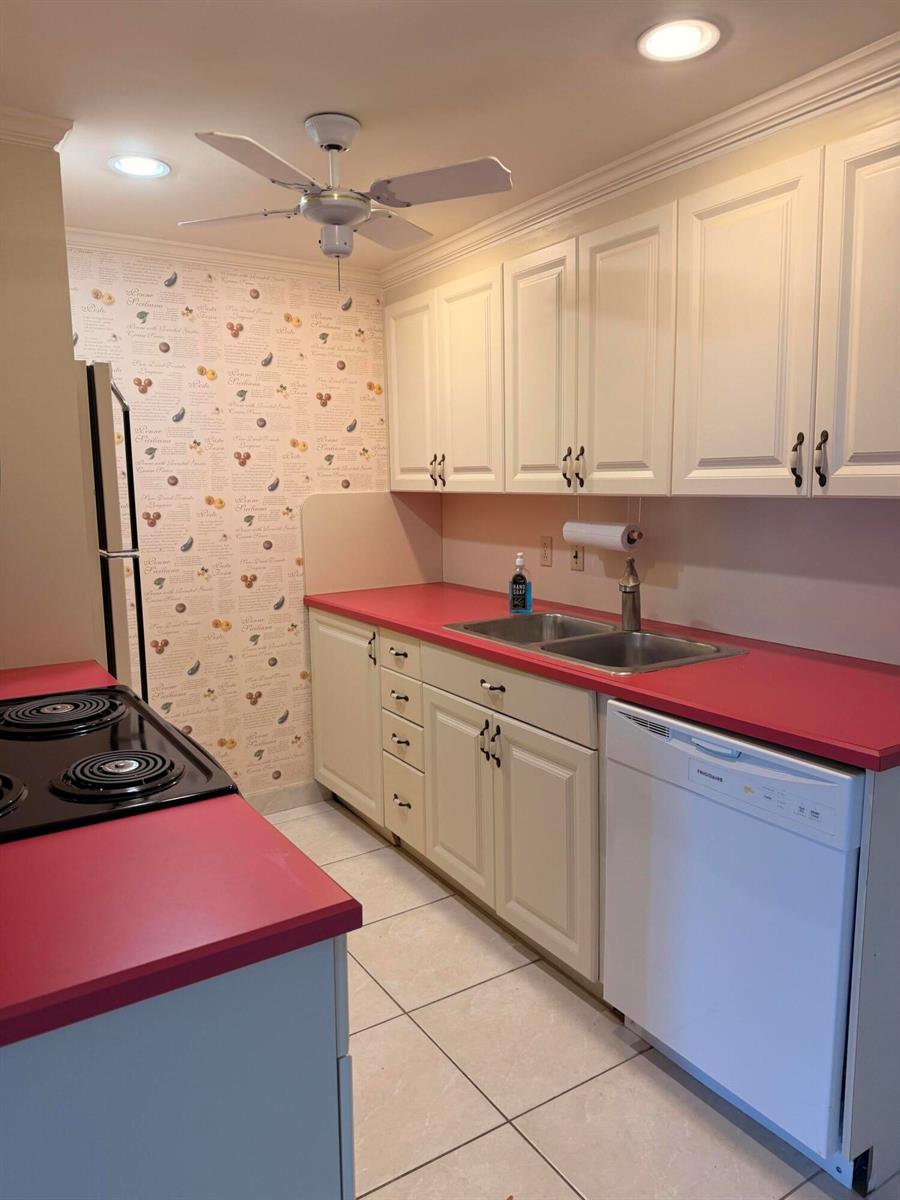A kitchen features white cabinets, a bright red countertop, patterned wallpaper, and a ceiling fan — 4074 Cornwall D, Boca Raton FL 33434, BOCA RATON, FL
